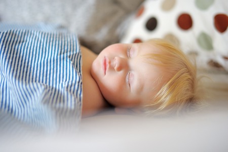 Adorable toddler boy sleeping in a bedの写真素材