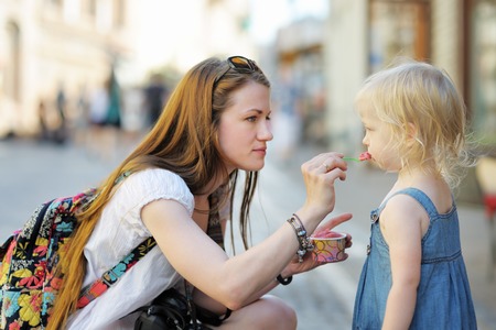 Young mother and her daughter eating ice cream outdoorsの写真素材