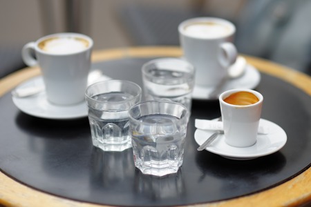 Three cups of fresh coffee (espresso and latte) and three glass with still water on table of Parisian outdoors cafeの写真素材