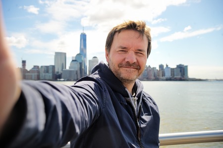 Middle age man taking a self portrait (selfie) with Manhattan skyscrapers in New York Cityの写真素材