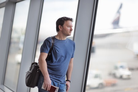 Male passenger at the airport with airplane on background. Middle age businessman holding passport and boarding pass.の写真素材