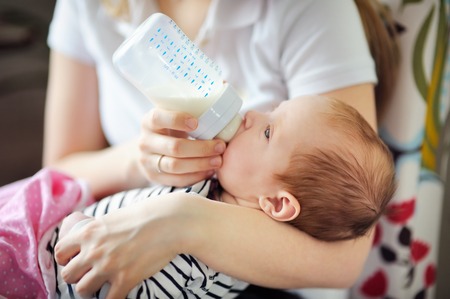 Adorable baby drinking milk from bottle in mother handsの写真素材