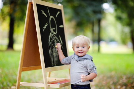 Beautiful toddler boy drawing standing by a blackboard outdoorsの写真素材