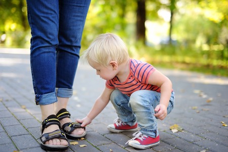Beautiful toddler boy playing with footwear at sunny parkの写真素材