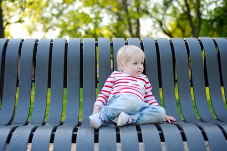 Toddler boy sitting on a bench outdoorsの写真素材