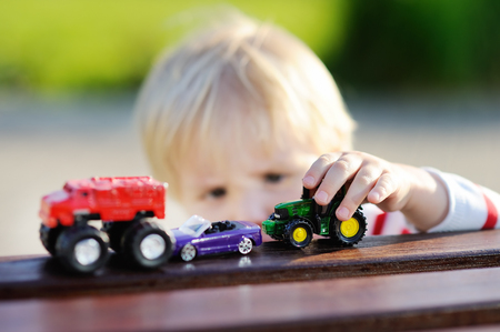 Cute toddler boy playing with toy cars outdoors at warm summer dayの写真素材