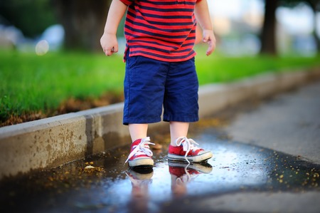 Toddler boy standing in a puddle on a warm summer or autumn dayの写真素材