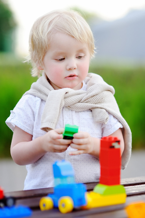Cute toddler boy playing with toy train and colorful plastic blocks outdoors at warm dayの写真素材