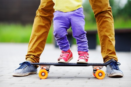 Cute toddler girl learning to skateboard with her father close up outdoorsの写真素材