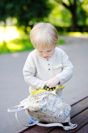Cute toddler boy putting his toys in backpack outdoorsの写真素材