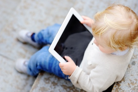 Cute blonde toddler boy playing with a digital tablet outdoorsの写真素材