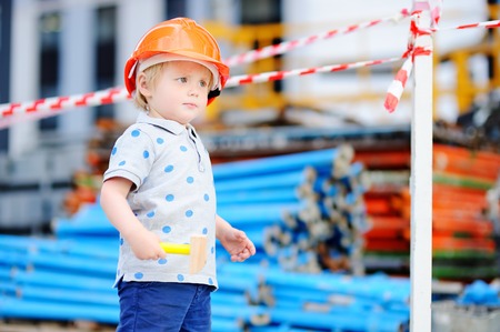 Portrait of serious little builder in hardhats with hammer working outdoorsの写真素材