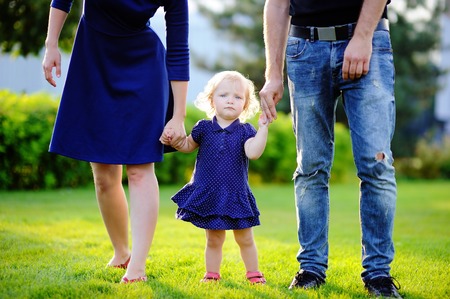 Happy parenthood: young parents with their sweet toddler girl in sunny park. The whole family dressed in the same color scheme. Family style clothing.の写真素材