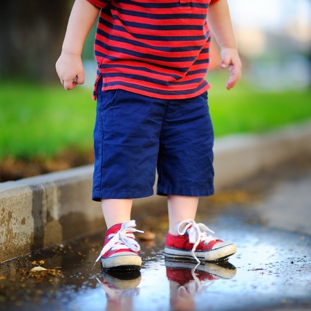 Toddler boy standing in a puddle on a warm summer or autumn dayの写真素材