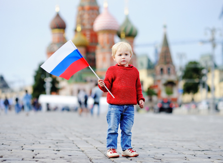 Cute toddler boy holding russian flag with Red Square and Vasilevsky descent on backgroundの写真素材