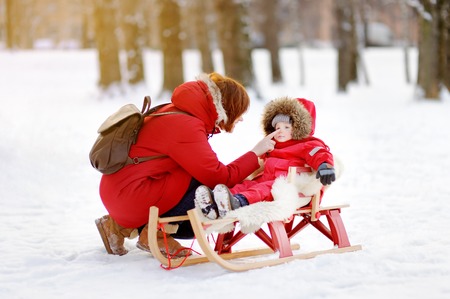 Portrait of beautiful toddler boy and his mother having fun in winter park. Family game with fresh...
