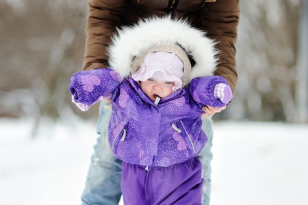 Little baby learning to walk. Young woman with her toddler girl at the winter parkの写真素材