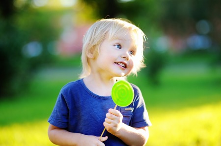 Cute toddler with big green lollipop. Child eating sweet candy bar. Sweets for young kids. Summer outdoor funの写真素材