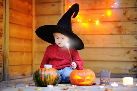 Cute little wizard playing with halloween pumpkins with lights on backgroundの写真素材