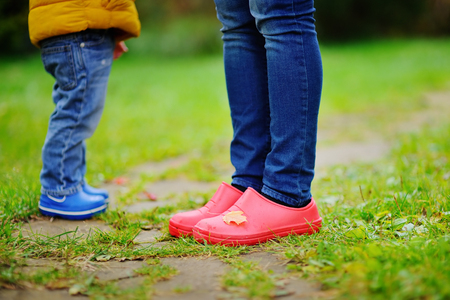 Close up photo of child and adult legs in rubber boots. Family in autumn.の写真素材