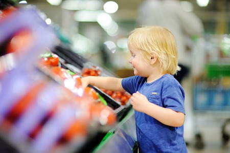 Cute toddler boy in a food store or a supermarket choosing fresh tomatoes. Healthy lifestyle for young family with kidsの写真素材