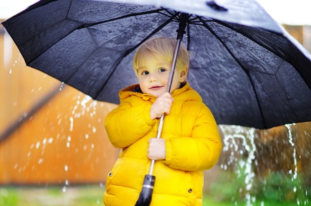 Little boy walking at rainy cloudy autumn weather. Child with big black umbrella in the rain. Fall outdoor activityの写真素材