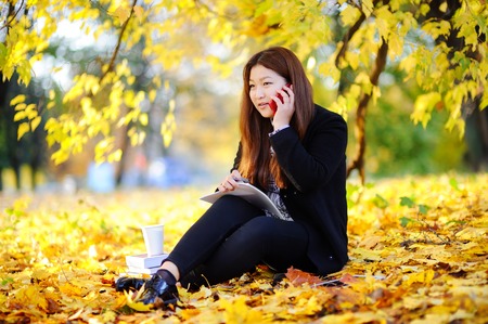 Beautiful asian student girl outdoors portrait. Young woman studying/working and enjoying beautiful sunny autumn dayの写真素材