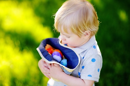 Little boy hunting for egg in spring garden on Easter day. Cute little child with traditional easter...