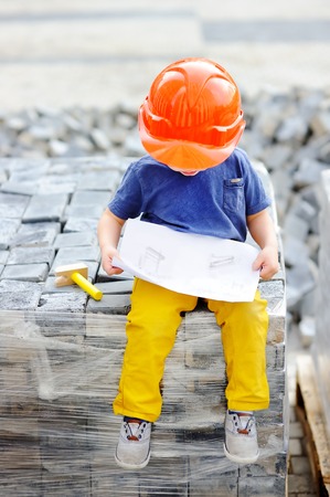 Portrait of cute little builder in hardhats reading construction drawing outdoors. Little boy's dream conceptの写真素材