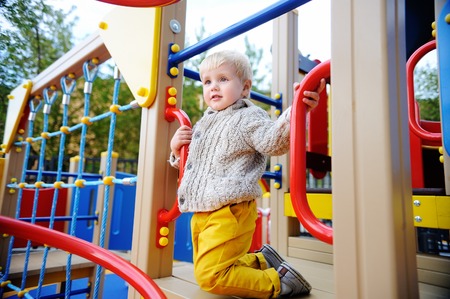 Cute toddler boy having fun on playground. Active outdoors game for little children