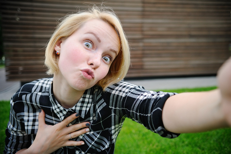 Young woman taking a outdoors self portrait (selfie) with smart phoneの写真素材