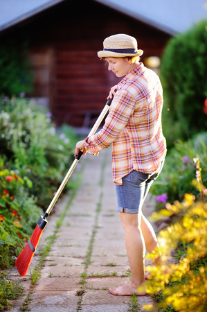 Middle age woman cleaning footpath in domestic garden in sunny summer dayの写真素材