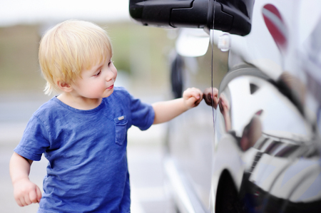 Pretty toddler boy see a new car of his father. Little child looking on his reflection in black minivanの写真素材