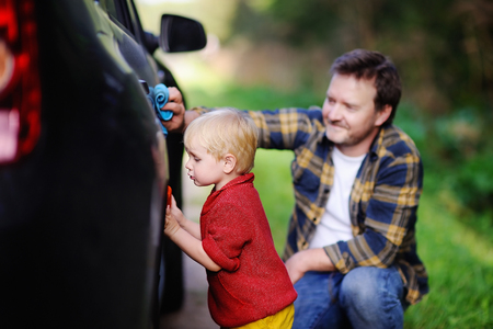 Middle age father with his toddler son washing car together outdoors. Family together activityの写真素材