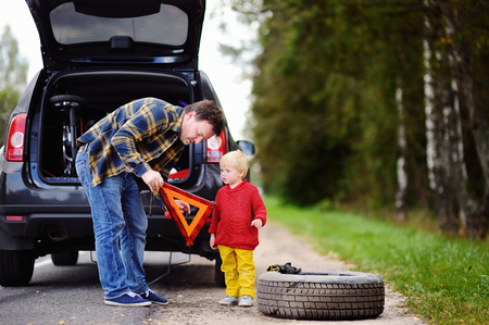 Father and his little son repairing car and changing wheel together on summer day. Family of two waiting car repair on the roadsideの写真素材