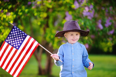 Cute toddler boy holding american flag in beautiful park. Independence Day concept.の写真素材