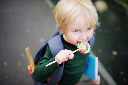 Cute little schoolboy outdoors on sunny autumn day. Young student with his backpack and lollipop. Education for small kids. Back to school concept.の写真素材