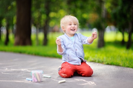 Happy little kid boy drawing with colored chalk on asphalt. Creative leisure for toddler child in summer park. Street art, kids education.の写真素材