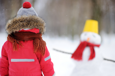 Little boy in red winter clothes having fun with snowman. Active outdoors leisure with children in winter. Kid during stroll in a snowy winter parkの写真素材