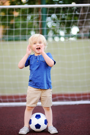 Little boy having fun playing a soccer/football game on summer day. Active outdoors game/sport for children. Kids soccer classes and campsの写真素材