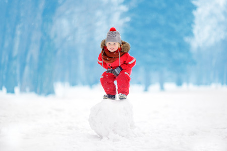 Little boy in red winter clothes having fun with snowball. Active outdoors leisure with children in winter. Kid during stroll in a snowy winter parkの写真素材