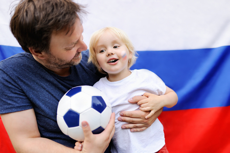 Portrait of little boy and his middle age father with russian flag on background. Fans child supporting and cheering their national team at the soccer/football sporting gamesの写真素材