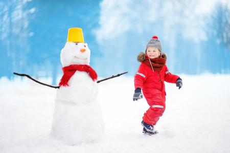 Little boy playing with funny snowman. Active outdoors leisure with children in winter. Kid during stroll in a snowy winter parkの写真素材