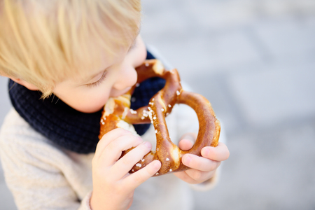 Little tourist eating traditional bavarian bread called pretzel in Munich, Germany. National cuisine conceptの写真素材