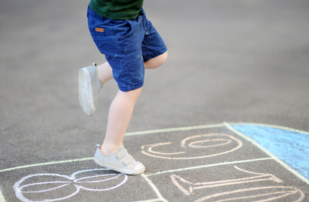 Closeup of little boy's legs and hopscotch drawn on asphalt. Child playing hopscotch game on playground outdoors on a sunny day. Summer activities for children.の写真素材