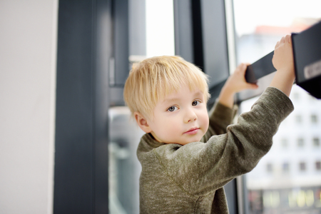 Lovely little boy sitting on the window near panoramic window and looking outside. Portrait of cute child with blonde hairの写真素材