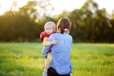 Young mother holding her little son during walk in the flowers field. Happy family together. Youthful tender mom with her cute toddler boy. Joyful motherhoodの写真素材