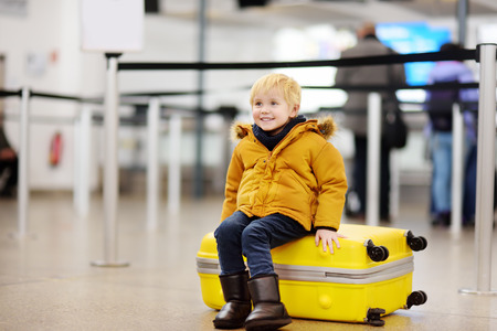 Cute little boy with big yellow suitcase at international airport before flight. Charming kid waiting boarding in terminal. Family travel with child conceptの写真素材