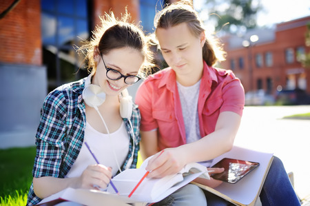 Young happy students with books and notes outdoors. Smart young guy and girl in University campus. Learning and education for young people.の写真素材