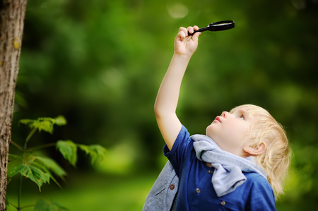Charming kid exploring nature with magnifying glass. Little boy looking at tree with magnifier. Summer activity for inquisitive childの写真素材
